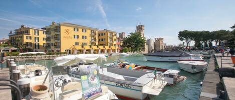 A marina with boats docked, a yellow building with balconies, and a tower in the background.