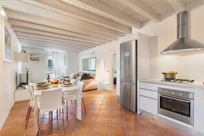 A modern kitchen with a built-in oven, a stainless steel refrigerator, and a dining area with white furniture.