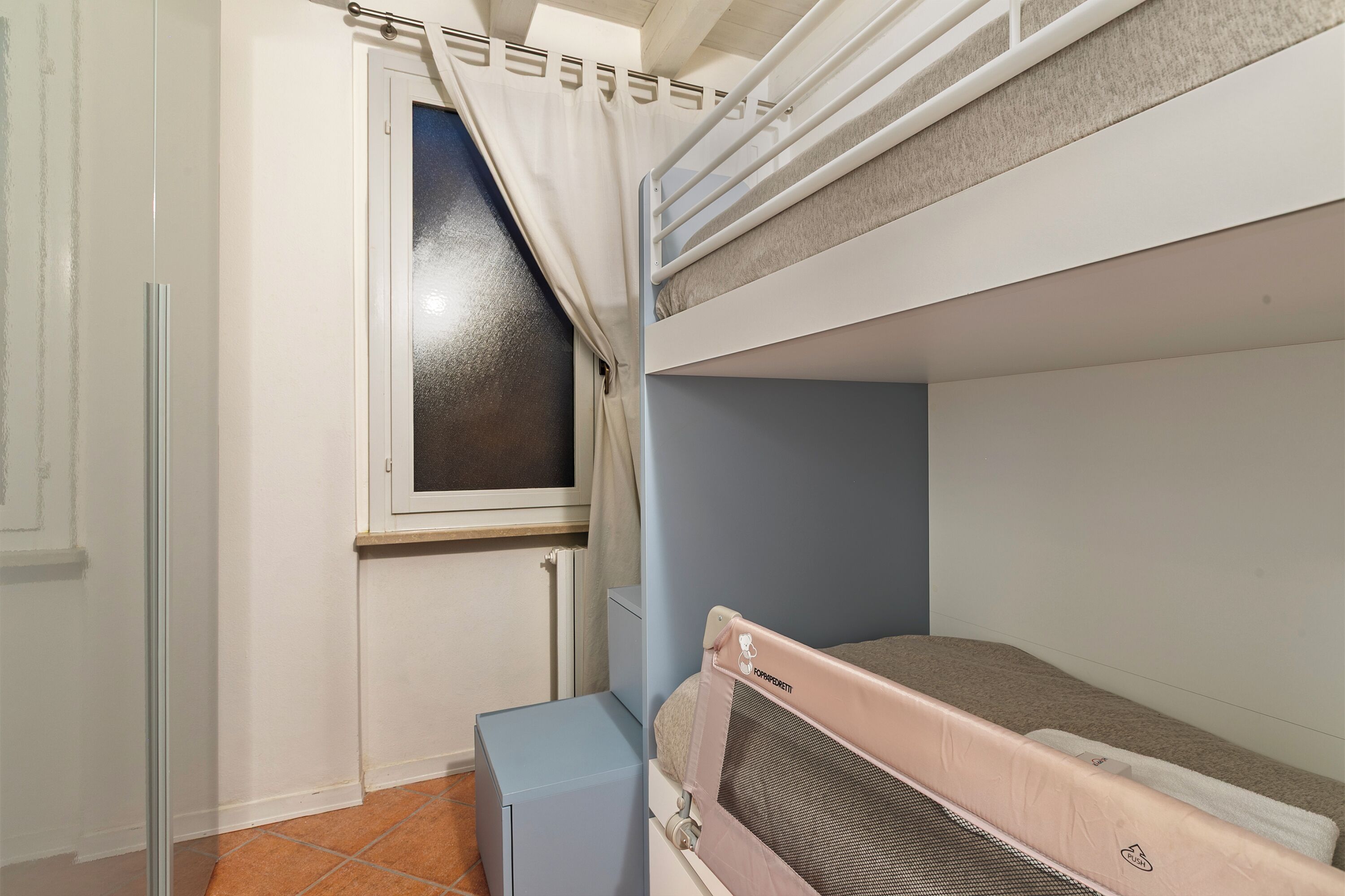 Une chambre avec un lit superposé, une fenêtre, un radiateur et un petit placard.