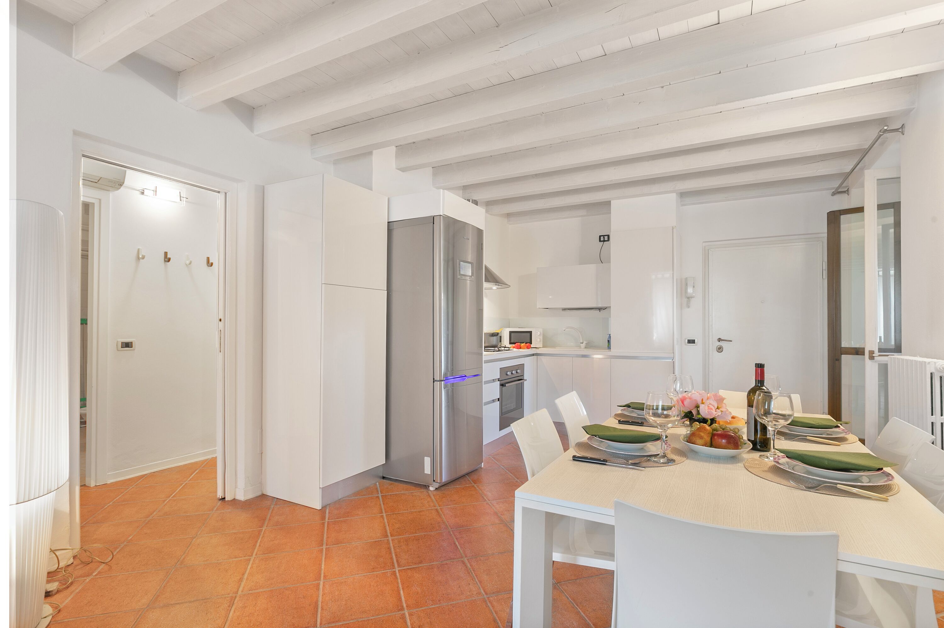 Une cuisine moderne avec des meubles blancs, un réfrigérateur en acier inoxydable et un coin repas avec une table dressée pour deux personnes.