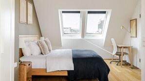A bedroom with a bed, a desk, and a chair. There is a window with a view of buildings. - Blueground | Josefstadt, terrace, nr Votivkirche (Vienna)