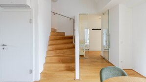A modern interior with a wooden staircase, a dining area with a table and chairs, and a mirrored wall. - Blueground | Josefstadt, terrace, nr Votivkirche (Vienna)