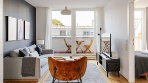 A modern living room with a grey sofa, a wooden chair, a small table, and a TV. - Blueground | Josefstadt, terrace, nr Votivkirche (Vienna)
