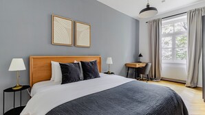 A bedroom with a large bed, two bedside tables, a desk, and a window with curtains. - Blueground | Alsergrund, view, nr Votivkirche (Vienna)
