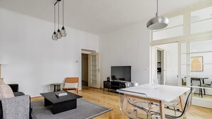 A modern living room with a sofa, coffee table, TV, and dining area. - Blueground | Alsergrund, view, nr Votivkirche (Vienna)