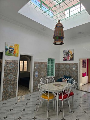 Un espace repas doté d’un plafond haut, de carreaux décoratifs, d’une lanterne suspendue et d’œuvres d’art accrochées aux murs.