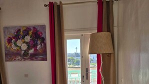 Ein Zimmer mit einer Couch, einem Gemälde, einer Lampe und einer zur Außenseite führenden Tür.