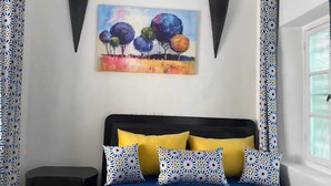 Ein Schlafzimmer mit einem Bett, einem Nachttisch, einem Gemälde und einem Vorhang mit Muster.