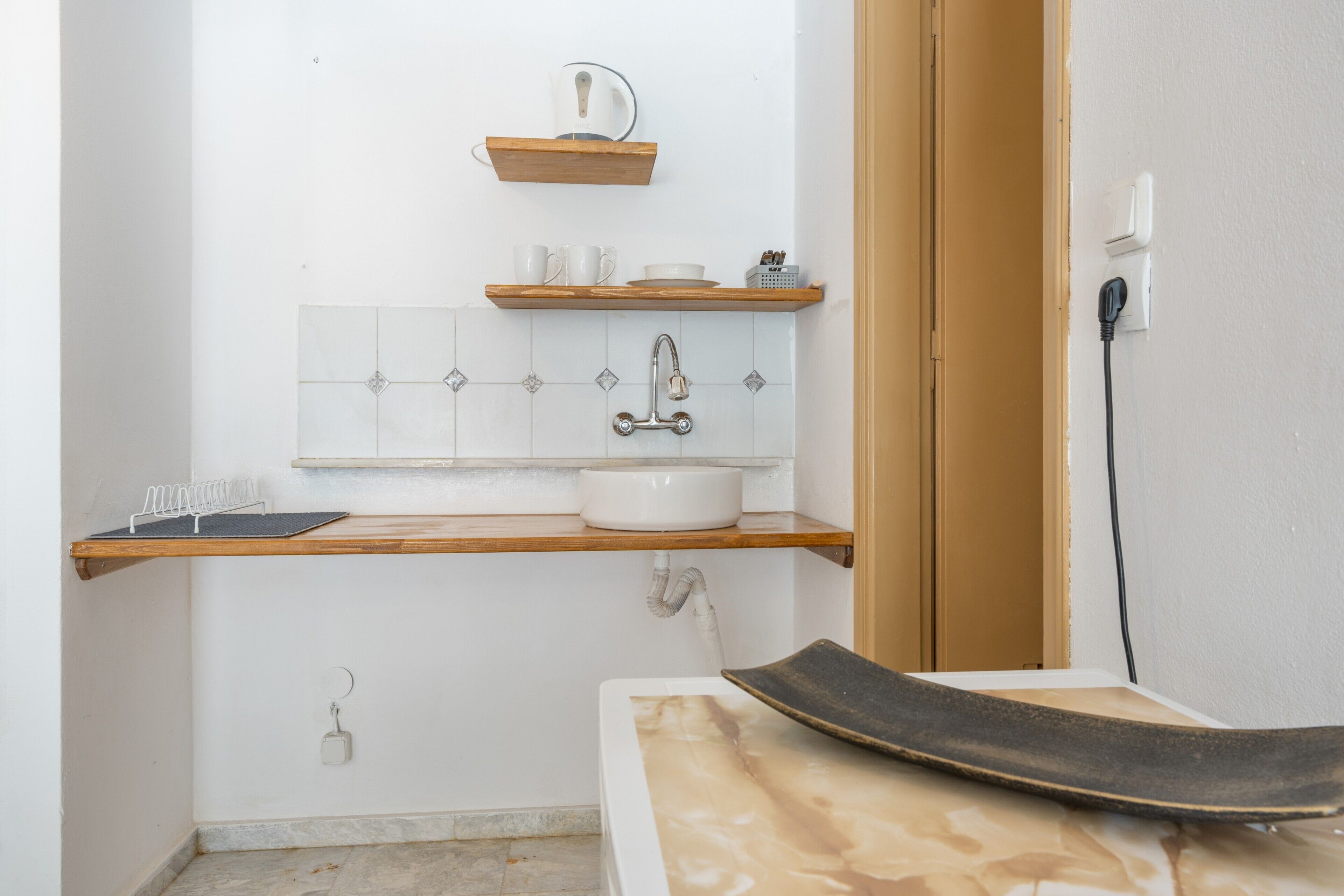 A bathroom with a white sink, wooden shelves, a towel rack, and a shower area.
