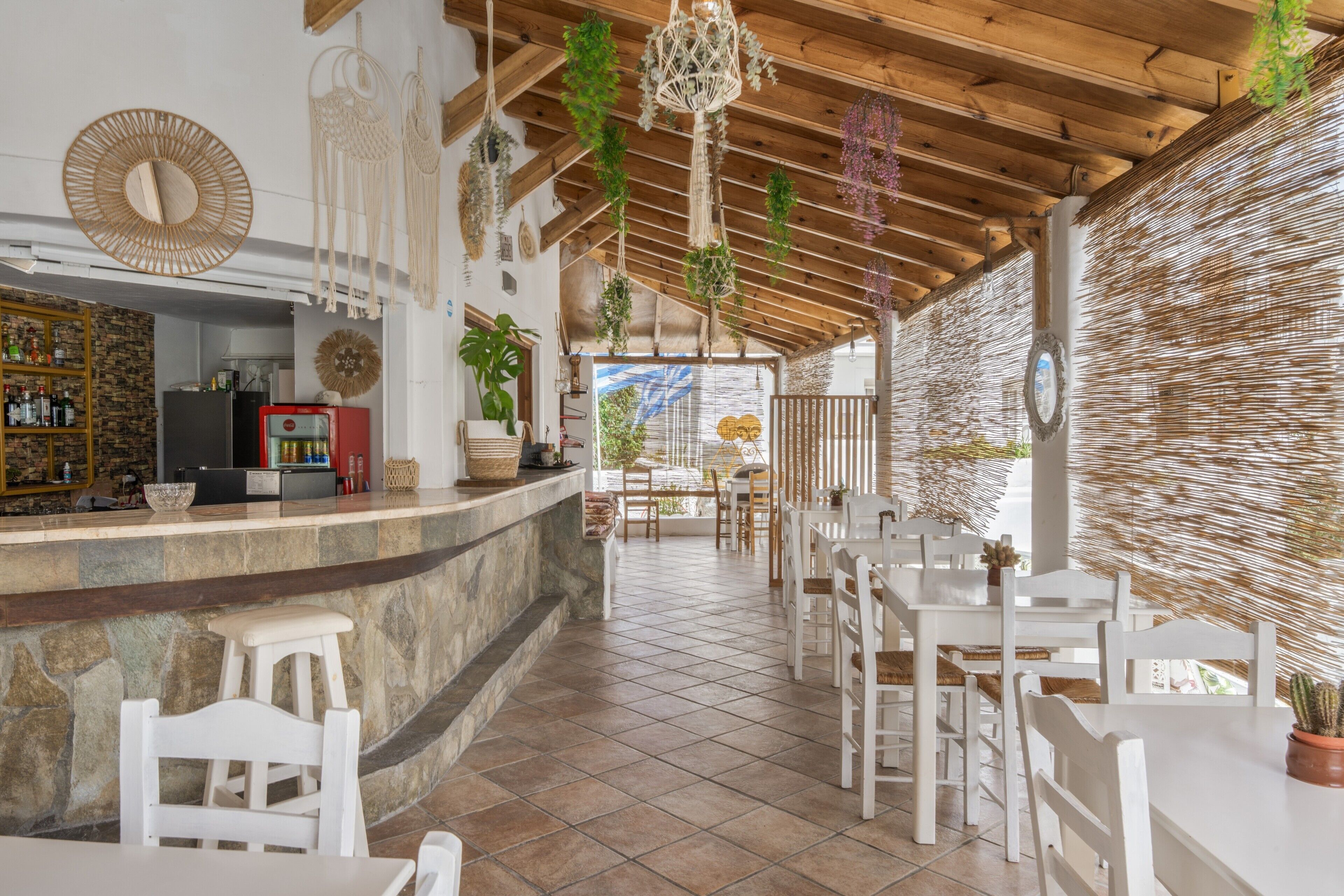 Un restaurant amb un taulell de pedra, caires blancs, plantes penjants i un sostre de fusta.