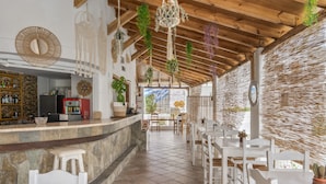 Un restaurant avec un comptoir en pierre, des chaises blanches, des plantes suspendues et un plafond en bois.