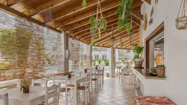 Un restaurant avec des tables et des chaises blanches, des plantes suspendues et un sol carrelé.