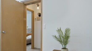 Ein Flur mit einer Holztür, einem kleinen Holztisch mit einem Blumentopf und einem Bett im Hintergrund.