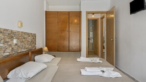 Ein Schlafzimmer mit Steinwand, Holzschrank, einem Bett mit weißer Bettwäsche, einem Nachttisch und einem an der Wand befestigten Fernseher.