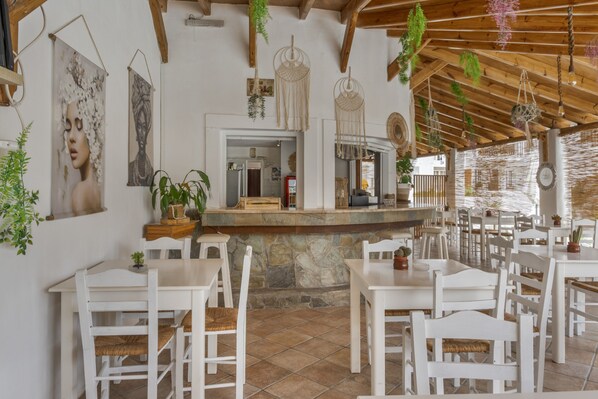 Un restaurant avec des tables et des chaises en bois peintes en blanc, un comptoir en pierre et des décorations en macramé suspendues.