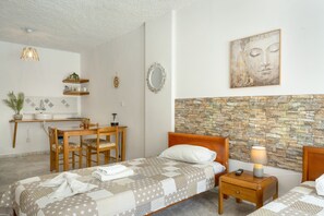 A hotel room with a bed, bedside table, a small desk with a chair, a mirror, and a Buddha painting on the wall.