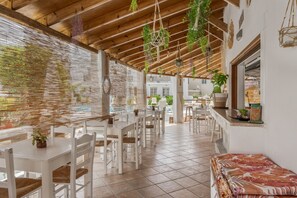 Un restaurant avec des tables et des chaises blanches, des plantes suspendues et un sol carrelé.