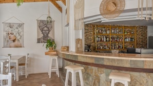 A bar area with a stone counter, white bar stools, a wooden ceiling, and a wall with framed artwork. - Apartment 'Room Pool View No 4' with Mountain View, Wi-Fi and Air Conditioning (Kalymnos)