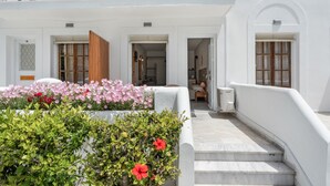 Ein weißes Gebäude mit Balkon, Treppe und Blumenbeet mit rosa und roten Blumen.