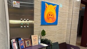 A reception area with a marble wall, a large pig painting, a reception desk with framed items, a purple sofa, and a black chair.