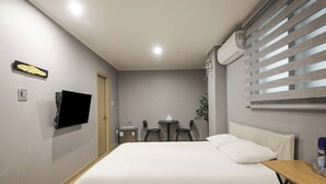 A hotel room with a bed, a TV, a desk, a chair, a small table, and a window with blinds.