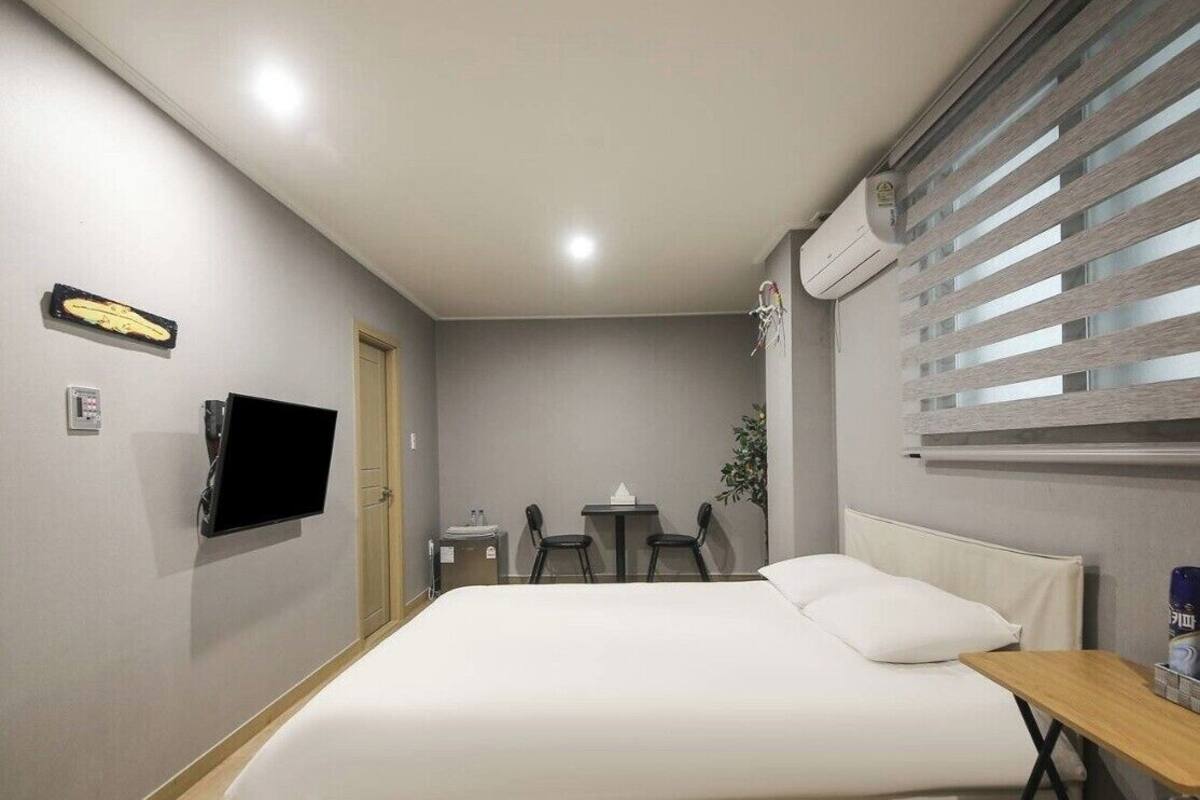 Une chambre d’hôtel comprenant un lit, une télévision, un bureau, une chaise, une petite table et une fenêtre avec des stores.