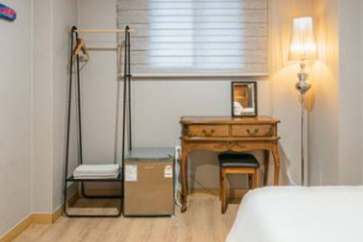 Une chambre à coucher comprenant un lit, un bureau avec une chaise, un appareil de musculation, une fenêtre avec des stores et une lampe de chevet.