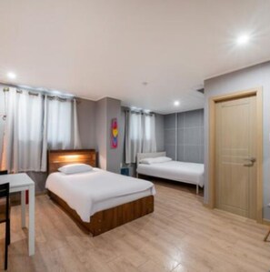 Ein Hotelzimmer mit einem hölzernen Bett, einem Schreibtisch und einem Sessel. Eine Tür und ein Fenster mit Vorhängen sind ebenfalls vorhanden.
