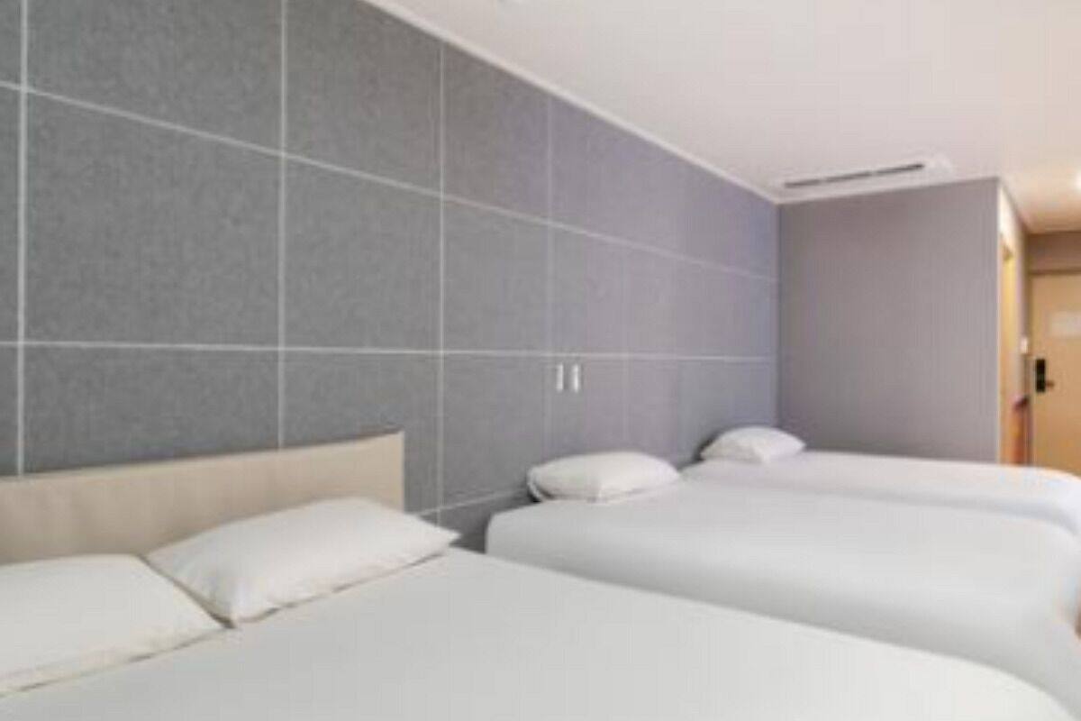 Une chambre d’hôtel avec un grand lit, une tête de lit et un mur recouvert de carreaux gris.
