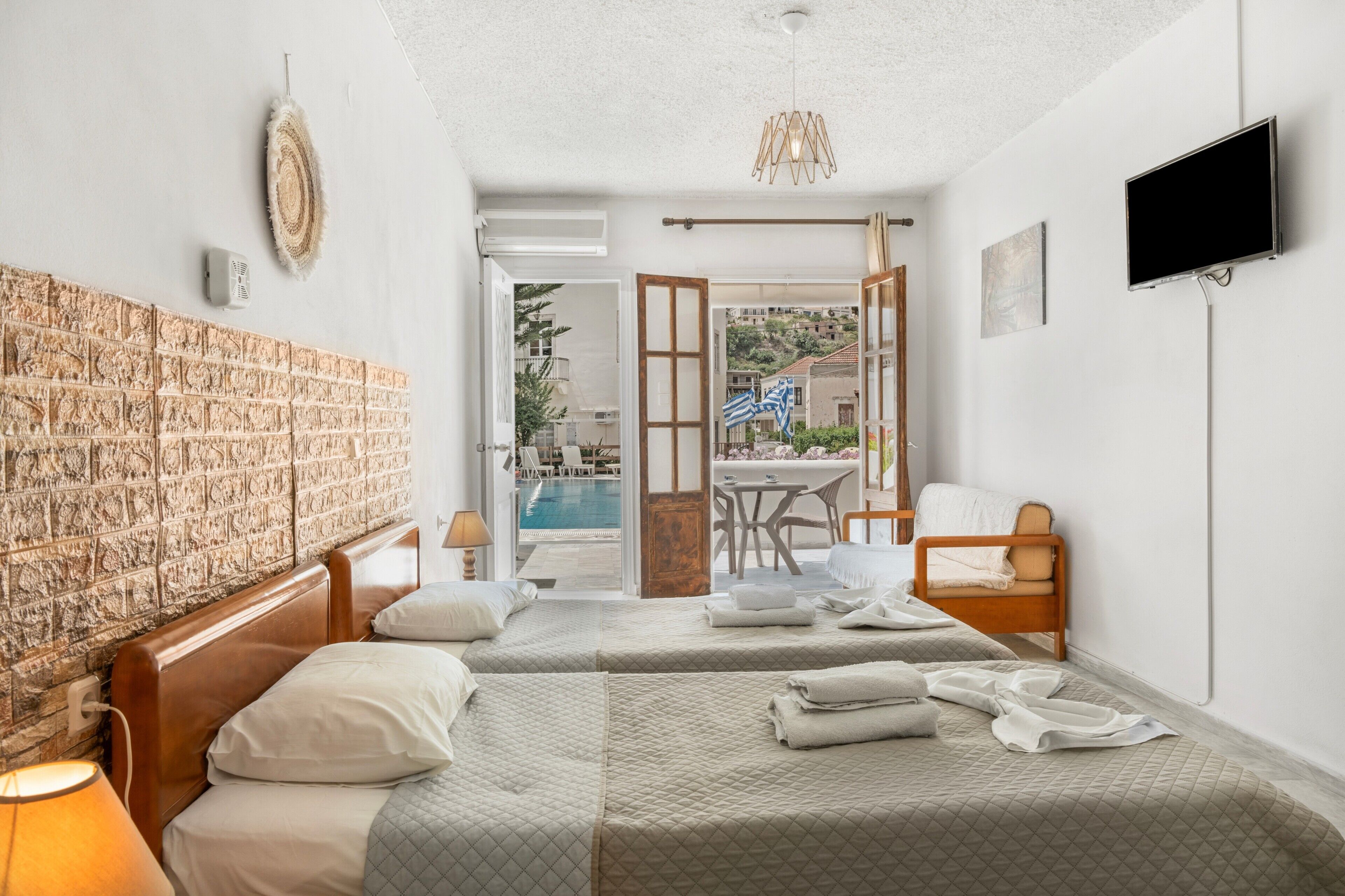 Habitación de hotel con dos camas, televisión, vista a la piscina y zona de comedor.