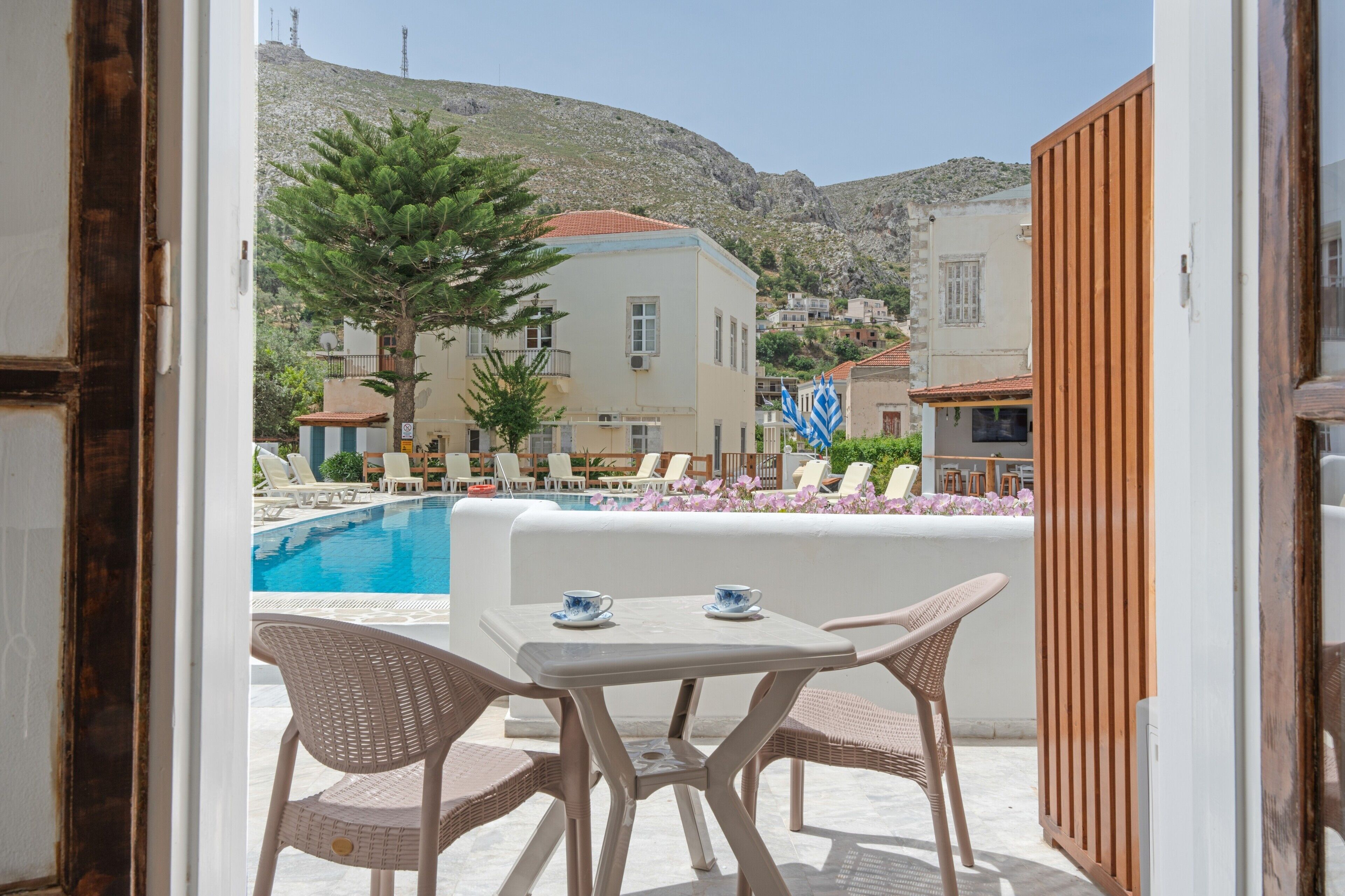 Uma área na piscina com espreguiçadeiras, uma mesa e vista para edifícios e uma montanha ao fundo.