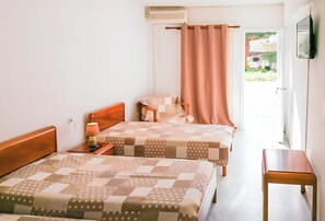 Une chambre avec deux lits, une table de chevet, une lampe, une fenêtre avec un rideau et une vue sur l’extérieur.