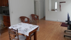 Un comedor con una mesa cubierta con mantel floral, dos sillas de madera y una cocina al fondo.