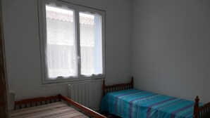 Una habitación con dos camas de madera, un radiador y una ventana que da a un tejado con tejas.