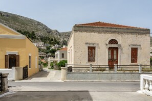 A street with buildings, a yellow building on the left, a white building with a red-tiled roof in the center, and a mountain in the background.