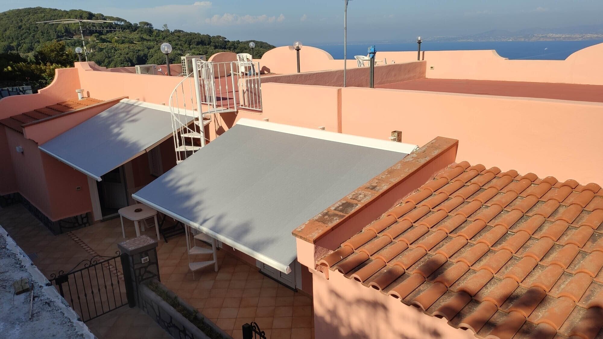 Eine Dachterrasse mit flacher Dachfläche, einem Abschnitt mit Ziegeldach und Blick auf das Meer.