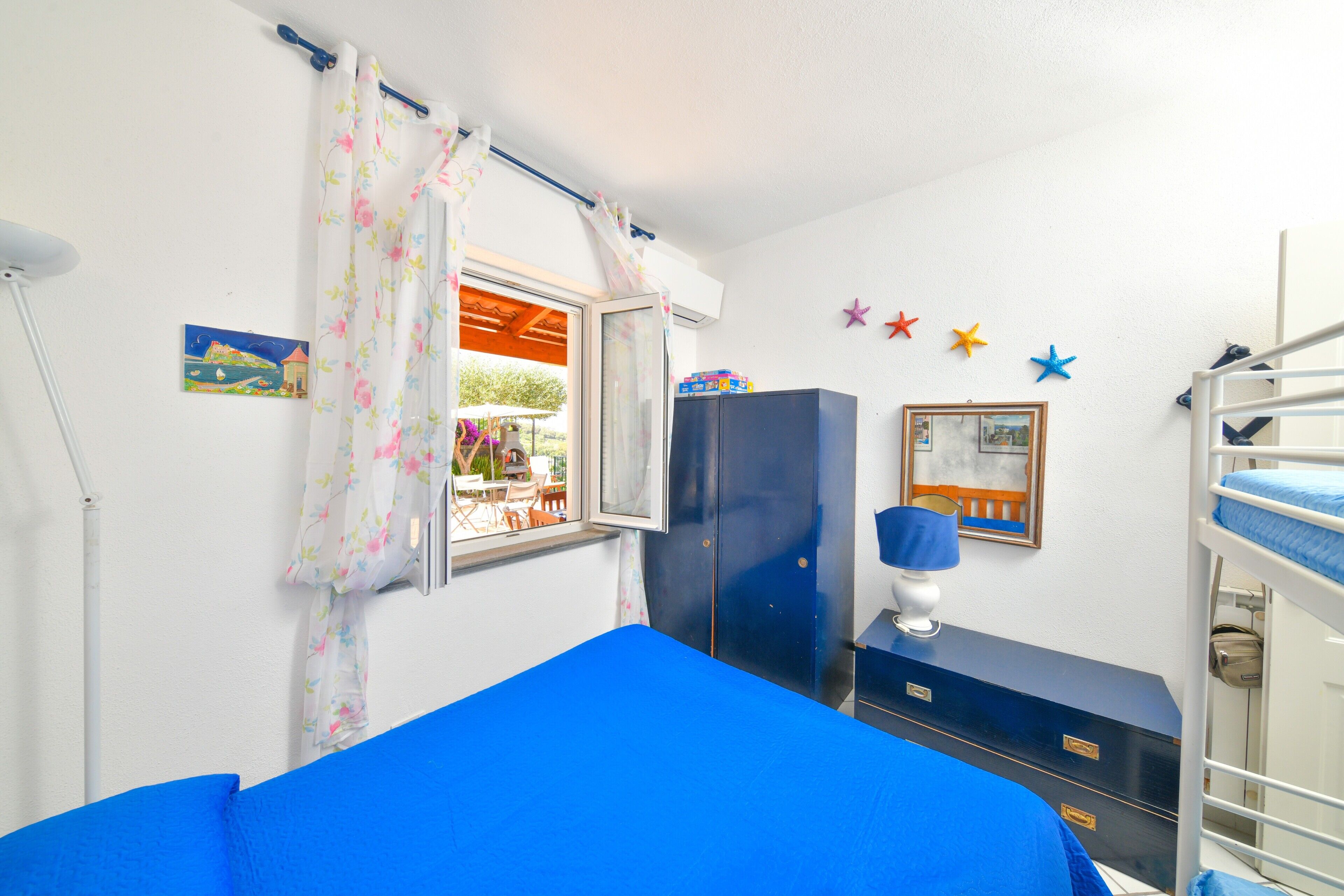A room with a bunk bed, a desk with a lamp, a wardrobe, and a window with curtains.
