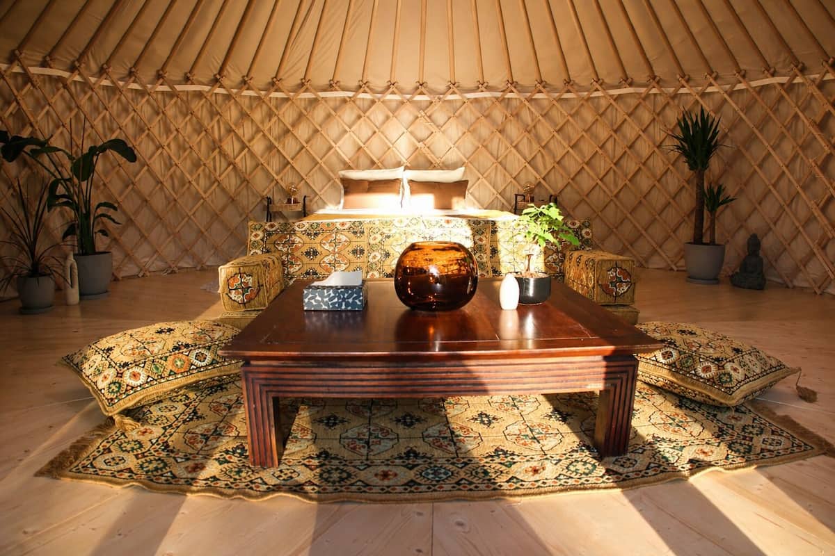 Una carpa con una mesa de madera, alfombras estampadas y plantas en macetas.