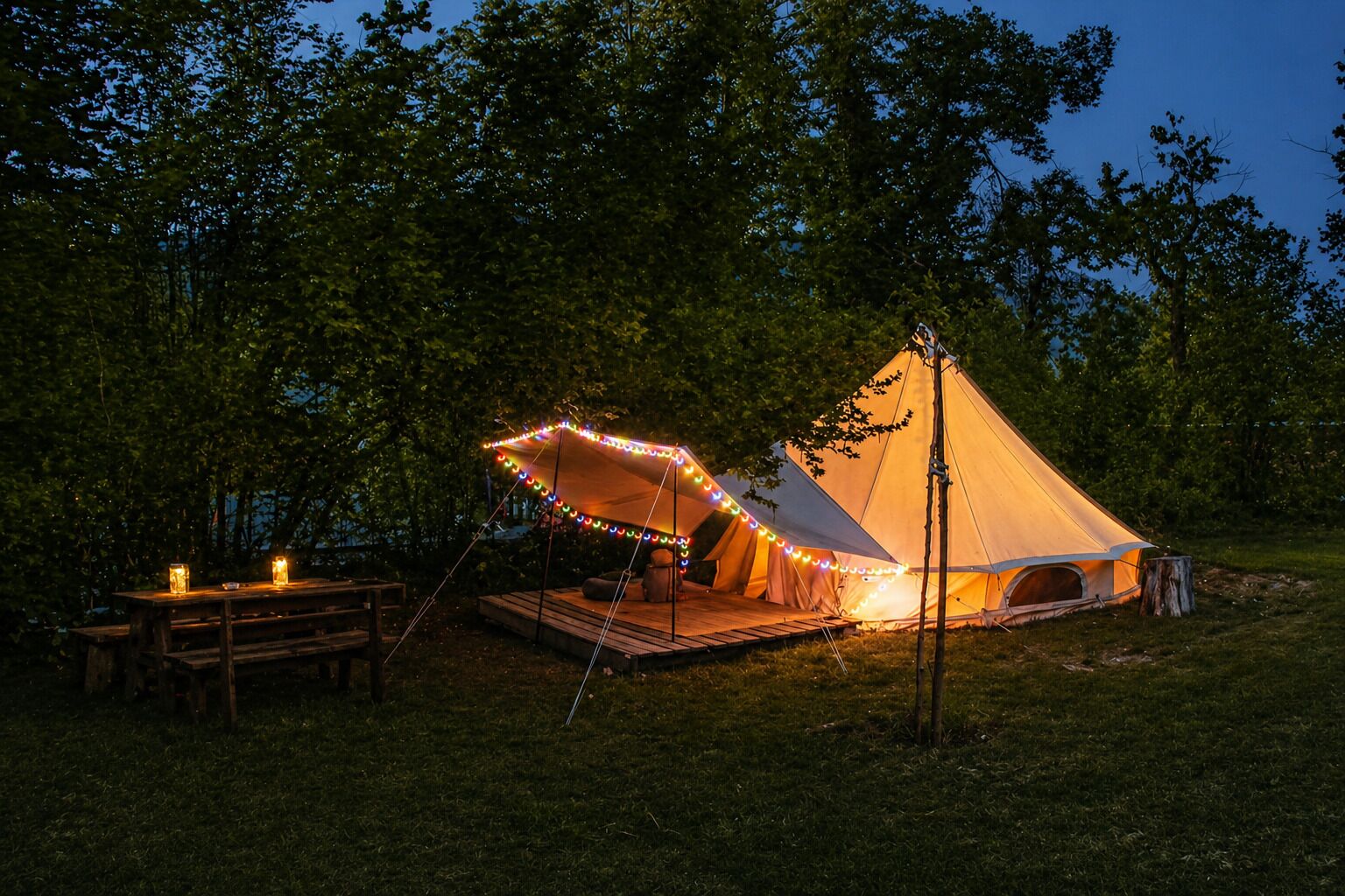 A tent with a platform and a table, surrounded by trees.
