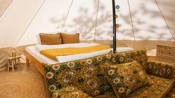 A tented accommodation with a bed, a sofa, and a small stool.
