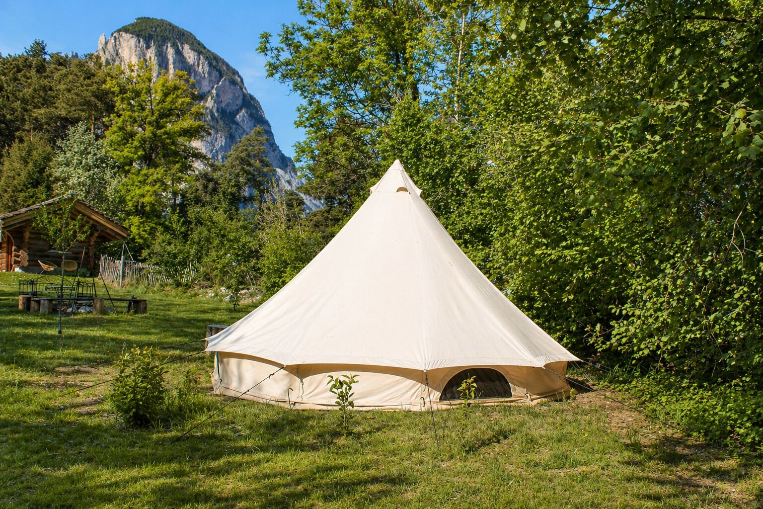A white tent-like structure in a grassy area with a mountain in the background.