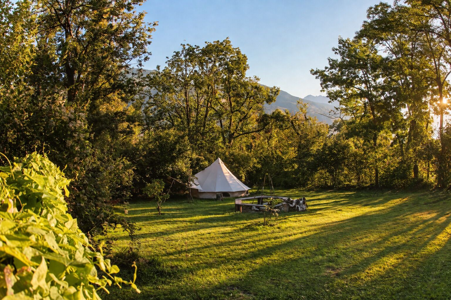 A tent in a grassy area with trees and mountains in the background.