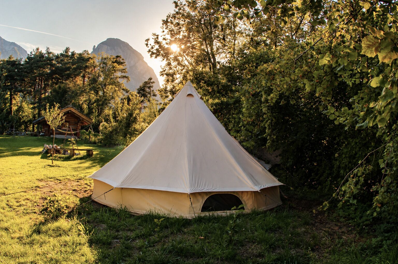 A conical tent in a grassy area with trees and a mountain in the background.