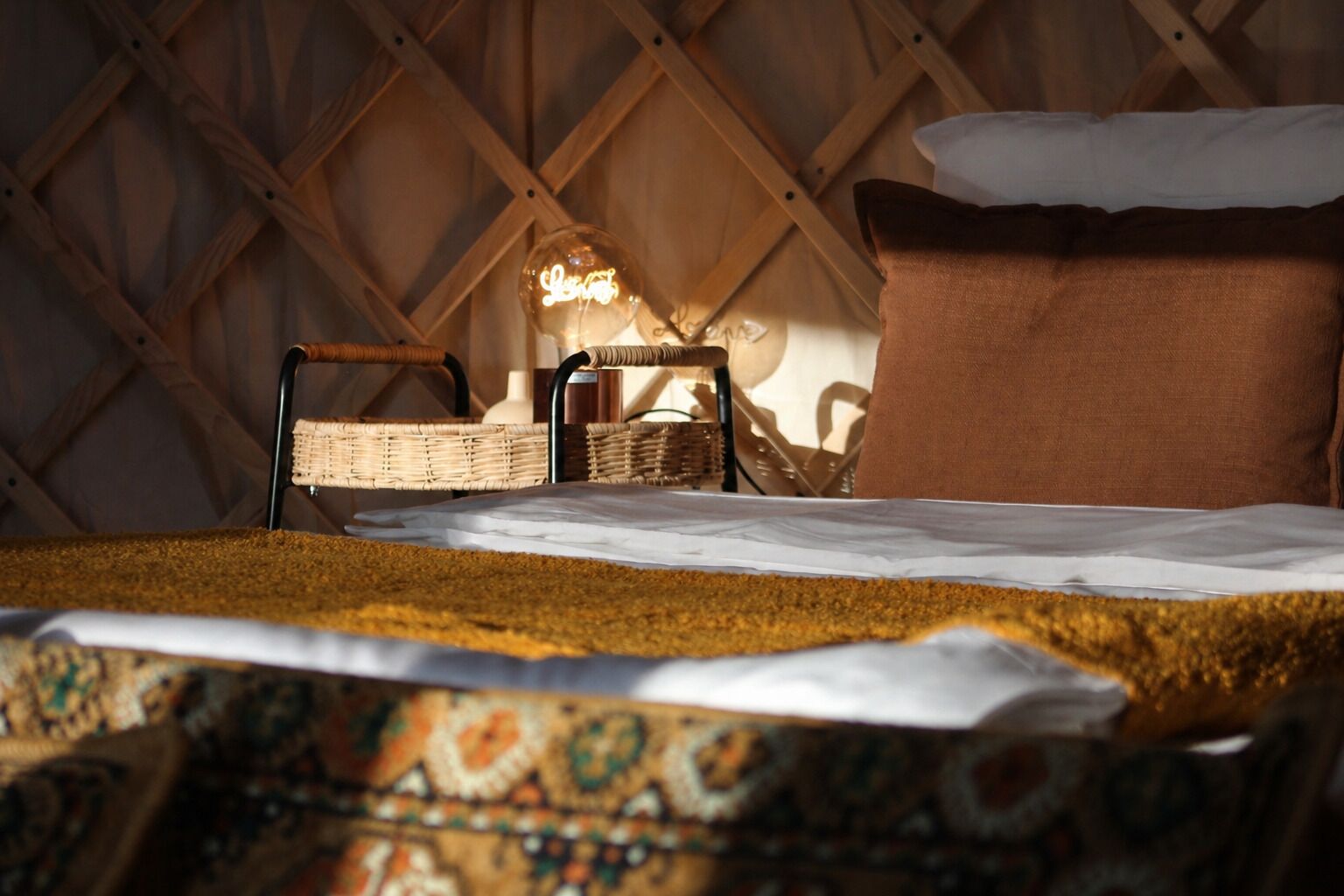 A cozy room with a bed, a wicker chair, a hanging light, and a wooden wall.