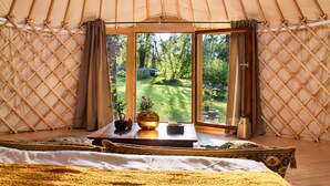 Ein geräumiges Zelt mit einer großen Schiebetür, einem Holztisch mit einer Vase und einem Buch, sowie ein Bett mit einer gelben Decke.