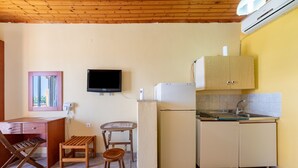 Una cocina compacta con techo de madera, televisor, refrigerador, lavamanos y un pequeño comedor.