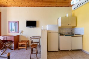A compact kitchen with a wooden ceiling, a television, a refrigerator, a sink, and a small dining area.
