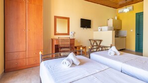 Habitación de hotel con dos camas, un armario de madera, un escritorio con silla, televisión y kitchenette.