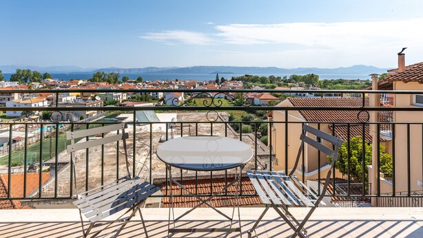 Un balcón con mesa y sillas, con vistas a una zona residencial con casas y un campo deportivo.