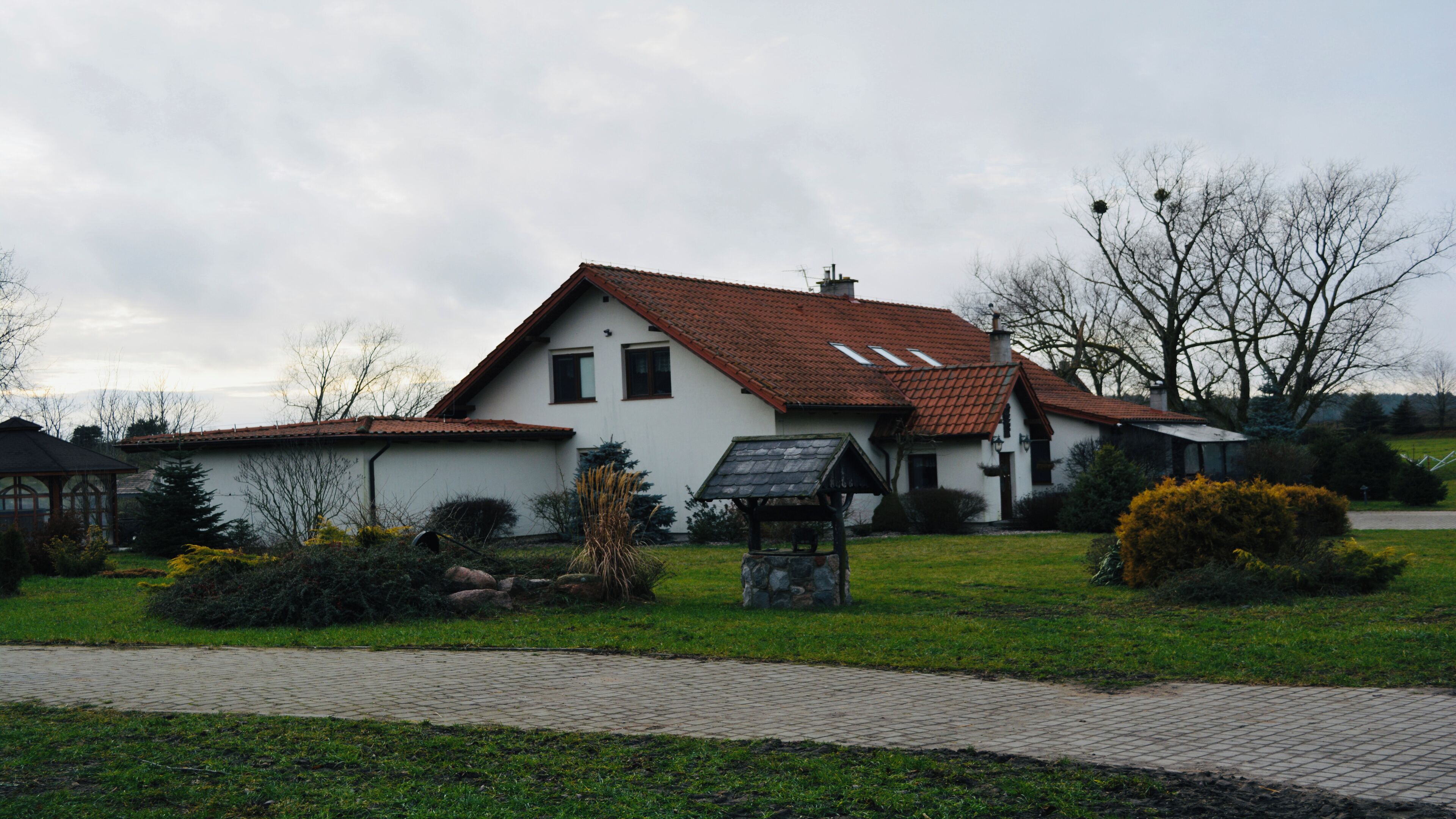 A white building with a red-tiled roof, a stone bench, and a paved walkway.